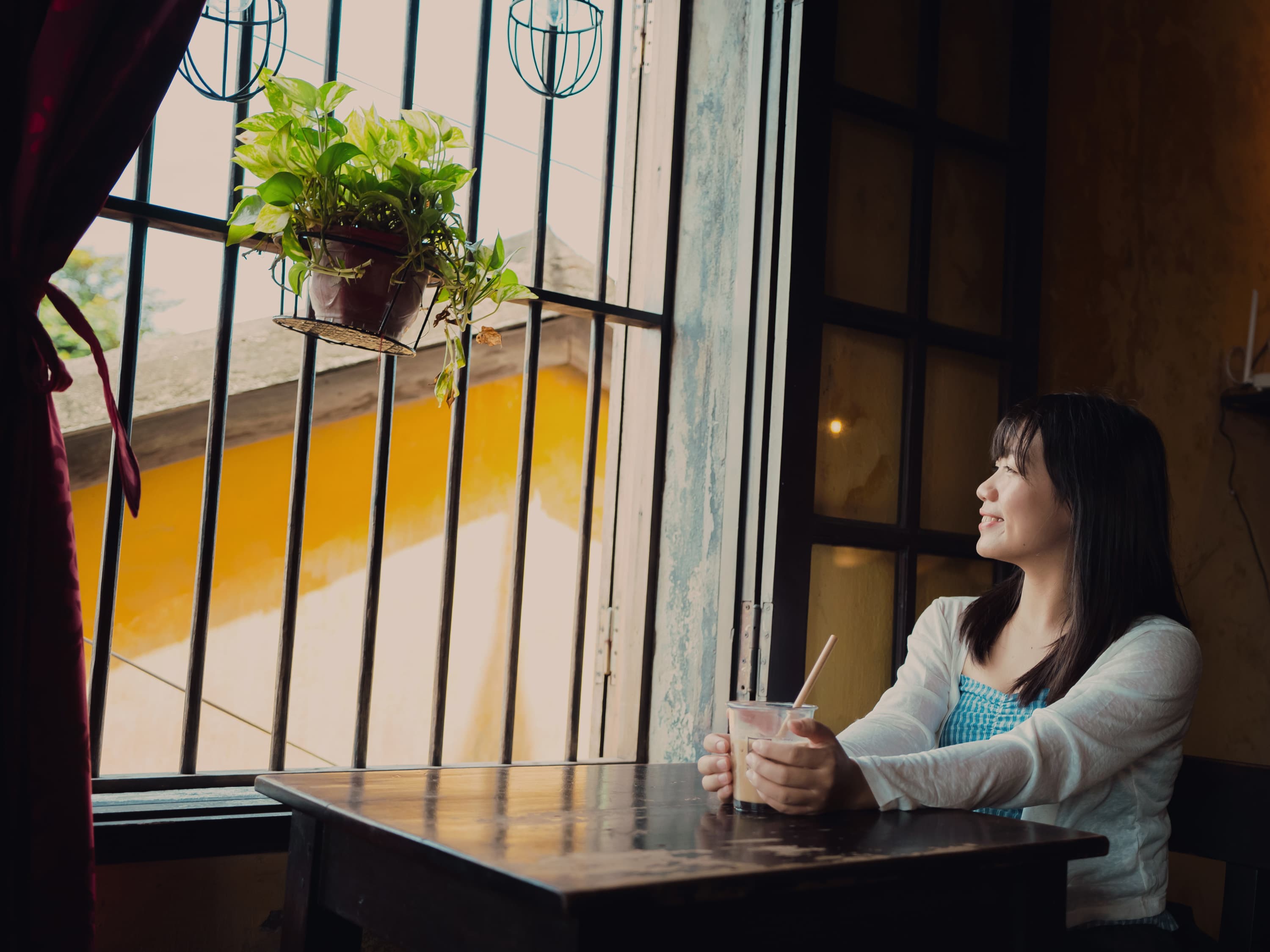 Xuân ngồi bên cửa sổ quán cà phê, cầm một ly nước mát