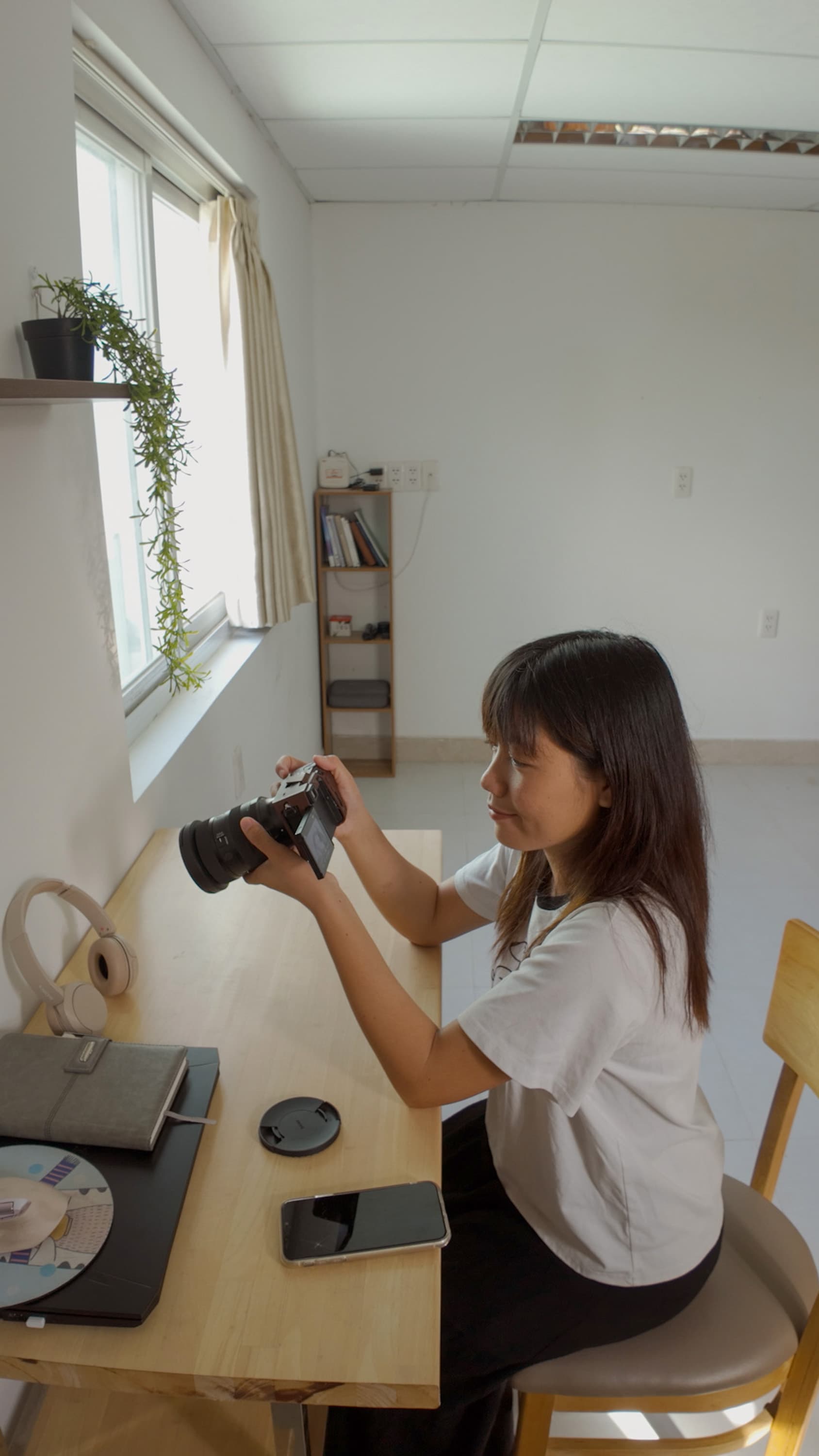 Xuân ngồi ở bàn làm việc, kiểm tra chiếc máy ảnh của mình