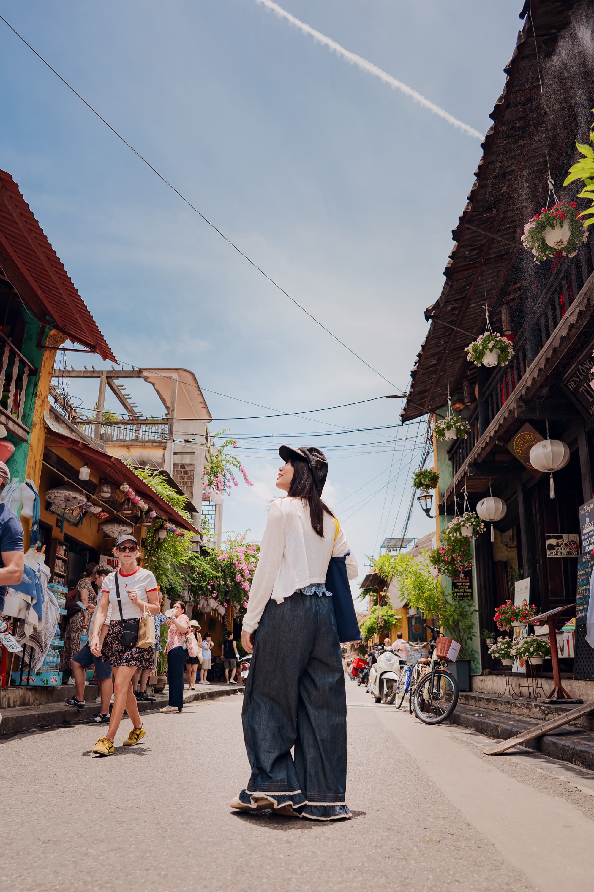 Xuân đứng giữa con phố cổ, ngước nhìn những mái nhà và đèn lồng