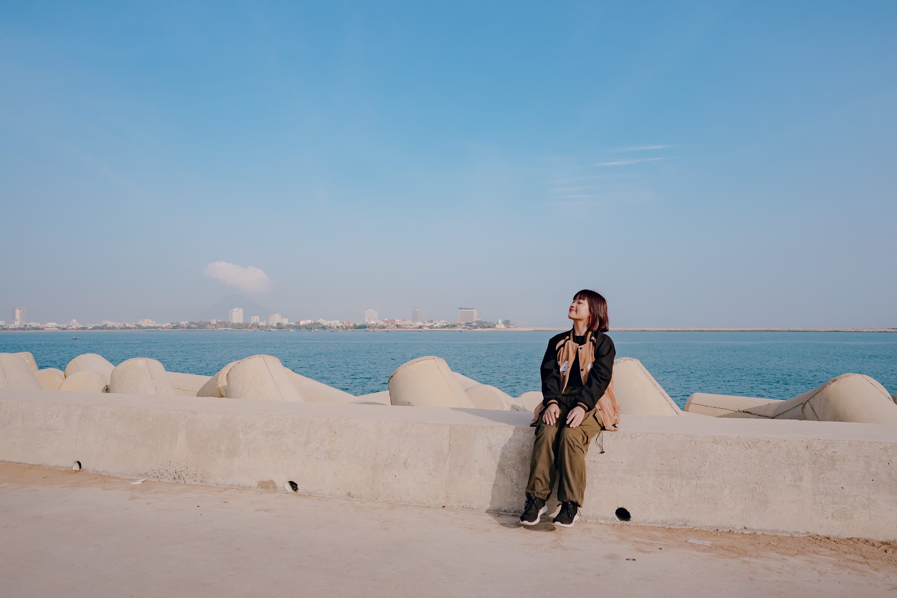 Xuân ngồi trên bờ kè, nhắm mắt tận hưởng nắng bên bờ biển